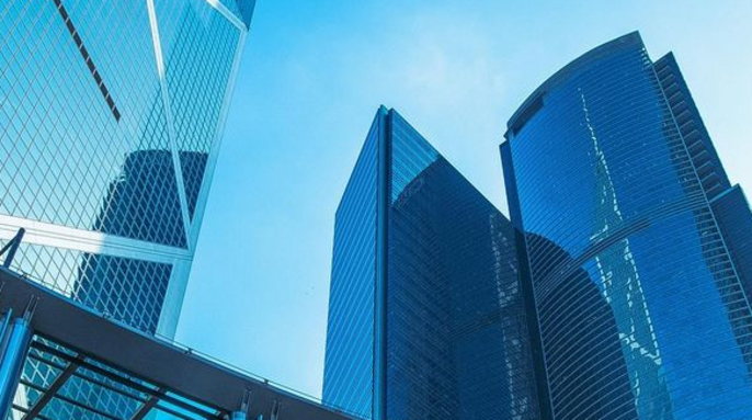 Drei moderne Wolkenkratzer mit spiegelnden Glasfassaden vor einem strahlend blauen Himmel.