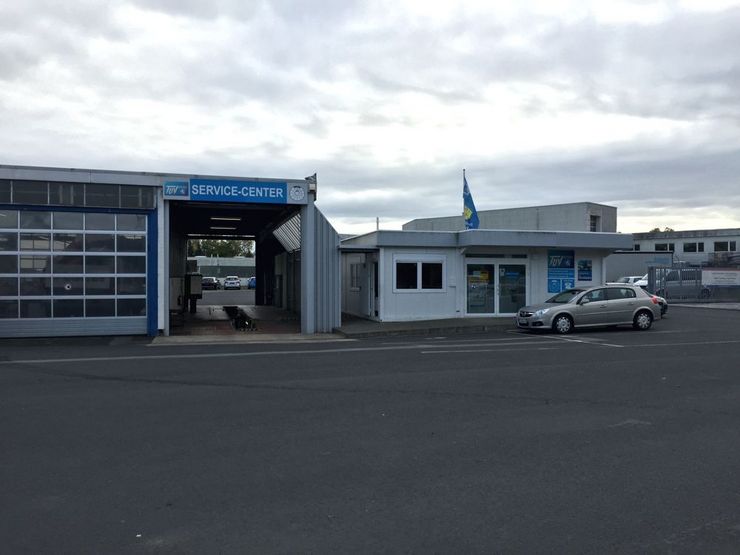 Eine Autowerkstatt mit einem blauen Schild mit der Aufschrift "TUEV Hessen SERVICE-CENTER", ein vor dem Haus geparktes Auto und ein Gebäude mit einer blauen Flagge.