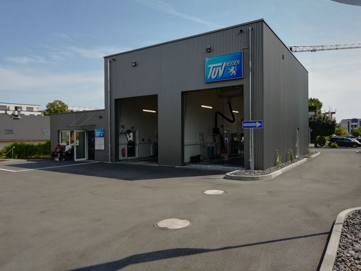Eine moderne Autowaschanlage mit einem Schild mit der Aufschrift "TUEV HESSEN", einer blauen Tür und ein paar geparkten Autos.