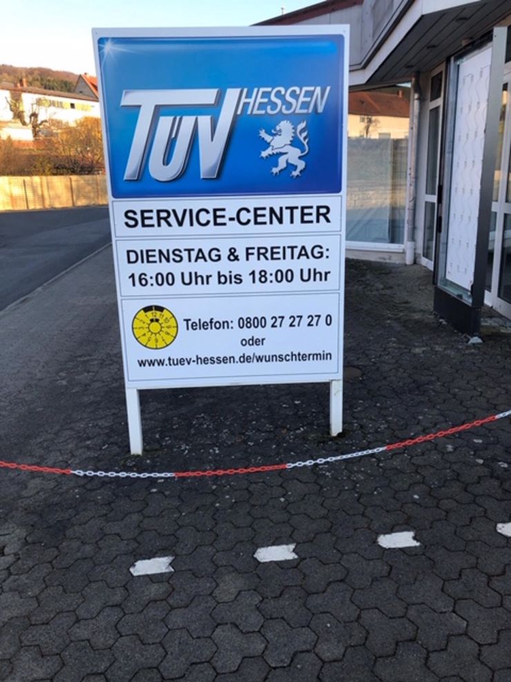 Ein Schild für "TUEV HESSEN" mit Angaben zum Service-Center, einschließlich Betriebszeiten und Kontaktinformationen.