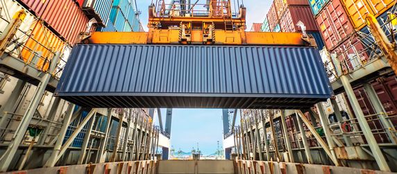 Ein Industriekran der einen Container in einem Containerlager hebt.