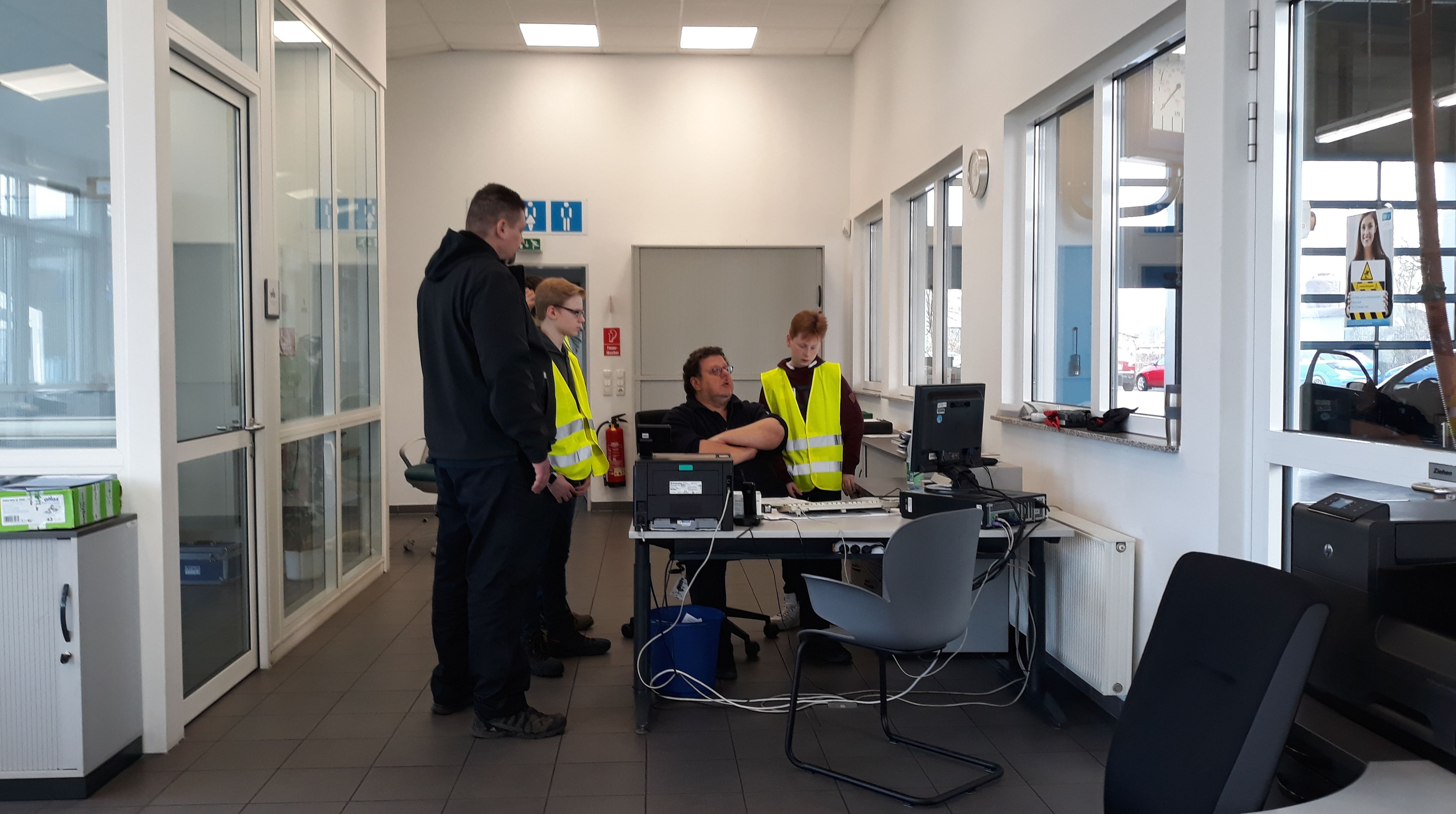 Ein modernes Büro, in dem vier Personen, von denen zwei Warnwesten tragen, an einem Computertisch eine Diskussion führen.