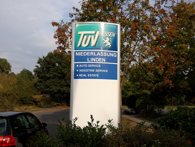 Ein Schild für 'TUEV HESSEN' mit Beschreibungen für 'Niederlassung', 'Auto Service', 'Industrie Service' und 'Immobilien'.