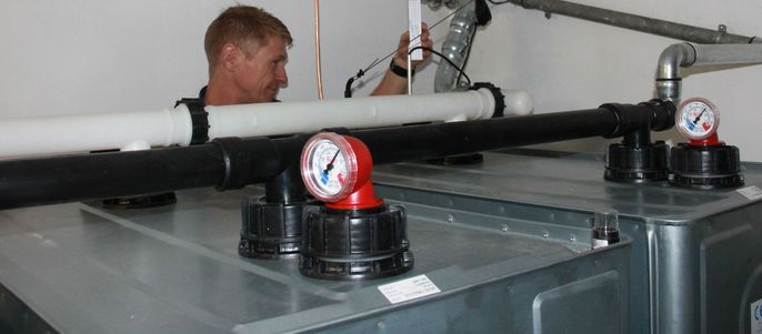 Ein Mann arbeitet an einem Sanitärsystem, mit verschiedenen Rohren, Ventilen und Manometern im Hintergrund.