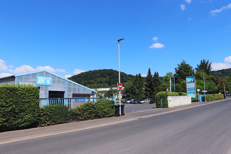 Ein blaues Industriegebäude mit der Aufschrift "TUEV Hessen", umgeben von Grünflächen und einer Straße.