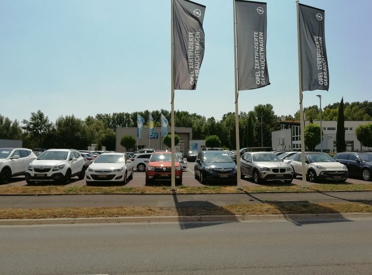 Ein Autohaus mit mehreren in einer Reihe geparkten Fahrzeugen, darunter drei große Werbebanner für Opel-Fahrzeuge.