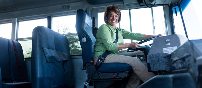 Eine Frau in einem grünen Hemd fährt einen Bus, angeschnallt.