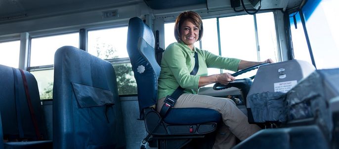 Eine Frau in einem grünen Hemd fährt einen Bus, angeschnallt.