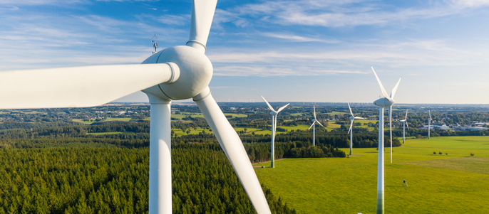 Eine weite Landschaft mit zahlreichen Windturbinen, die sich vor einem Hintergrund aus grünen Feldern und blauem Himmel erheben.