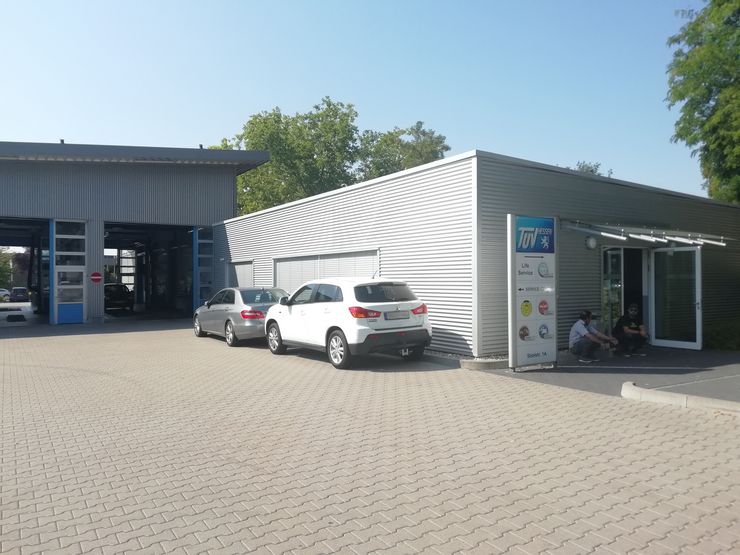 Ein modernes Autowerkstattzentrum mit einem weißen Auto, das draußen geparkt ist, einem blauen Schild mit verschiedenen Dienstleistungen und ein paar Personen, die draußen sitzen.