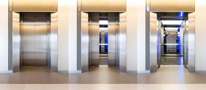 Drei Aufzugstüren, von denen die mittlere geöffnet ist und einen blau beleuchteten Innenraum freigibt.