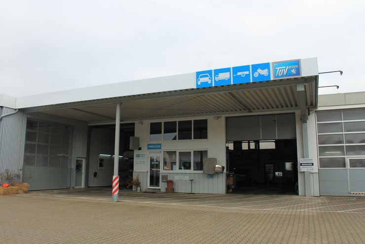 Ein modernes Autowerkstattzentrum mit einem blauen Schild mit der Aufschrift "TUEV", einem Schalter mit einer Person dahinter und ein paar geparkten Autos.