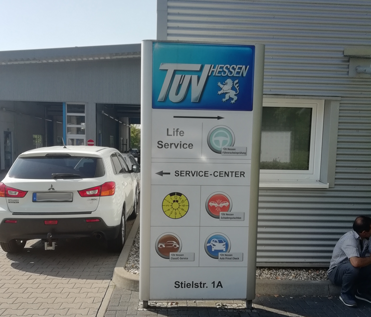 Ein Schild für eine Autowerkstatt namens 'TUEV HESSEN'. Das Schild zeigt den Weg zum Service-Center.