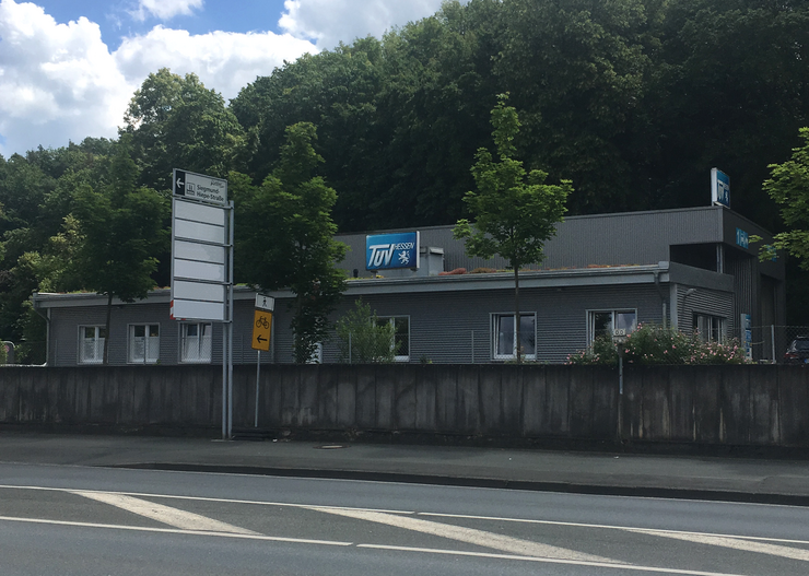 Ein Gebäude mit einem "TUEV Hessen"-Schild, umgeben von Bäumen und einer Straße.