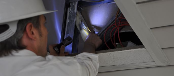 Ein Arbeiter der ein Untersuchung von Schadstoffen in einer Decke durchführt.