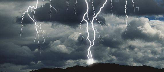 Ein Gewitter mit Blitzeinschlag über einem Wald.