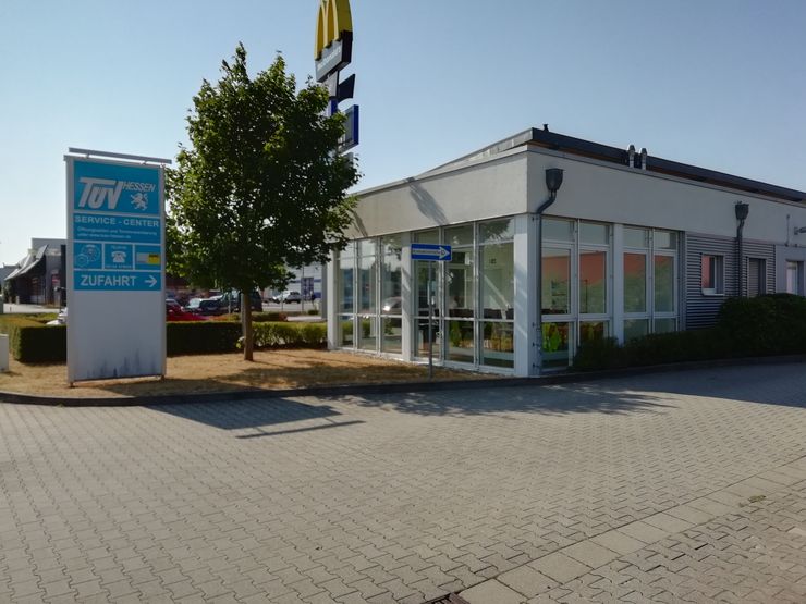 Ein modernes Gebäude mit einem "TUEV Hessen"-Service-Center-Schild und einem Baum im Vordergrund.
