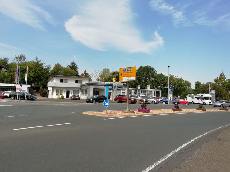 Ein Autohaus mit mehreren geparkten Autos, ein Gebäude mit dem Schild "Erlenhoff GmbH" und ein Schild mit einer Karte, die auf die "Erlenhoff GmbH" hinweist.