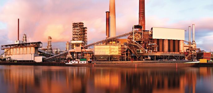 Eine industrielle Umgebung mit hohen Schornsteinen, Maschinen und einem ruhigen Gewässer, in dem sich die Strukturen spiegeln.