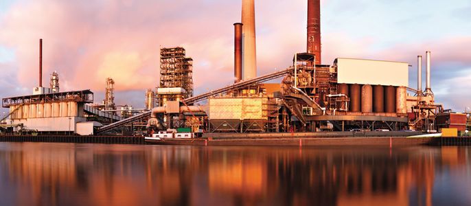 Eine industrielle Umgebung mit hohen Schornsteinen, Maschinen und einem ruhigen Gewässer, in dem sich die Strukturen spiegeln.