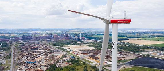 Ein Windrad, die in einem Industriegebiet mit verschiedenen Gebäuden und Infrastrukturen steht.