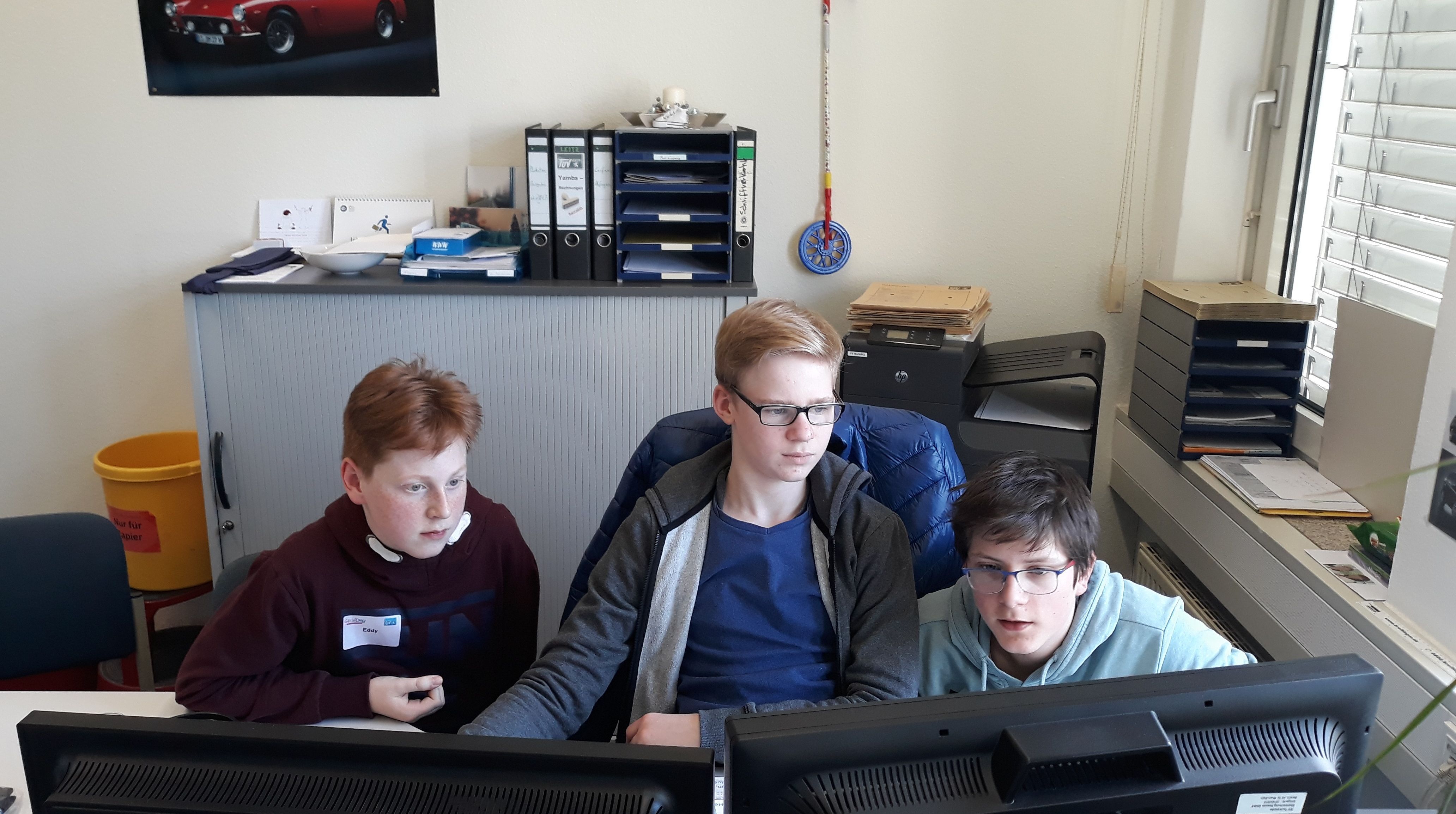Drei Jungen in einer Büroumgebung, die auf Computerbildschirme schauen.