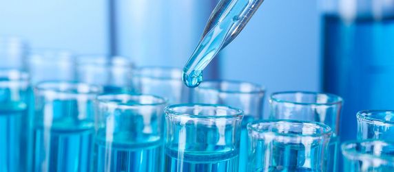 Eine Pipette die eine Flüssigkeit in Reagenzgläser träufelt.