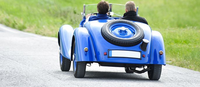 Oldtimer mit 2 Fahrenden bei Tag.