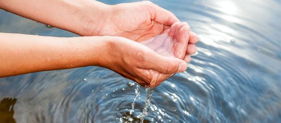 Person schöpft Wasser mit Händen.