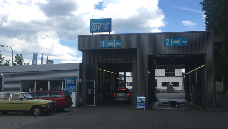 Eine zweispurige Autowaschanlage mit einem Schild 'TUEV Hessen' und ein paar geparkten Autos.