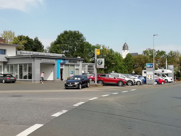Ein Autohaus mit einem TUEV Hessen Logo, mehreren geparkten Autos und einer Person, die in der Nähe des Eingangs geht.