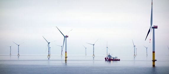 Eine weite, ruhige Wasserfläche mit mehreren Windturbinen, die sich am Horizont erheben, und einem Boot, das zwischen ihnen hindurchfährt.