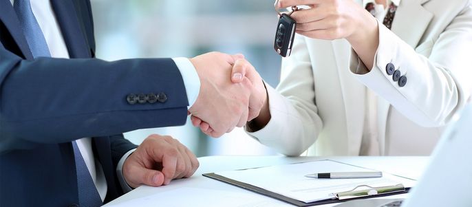 Ein Händedruck zwischen zwei Personen, bei dem die eine Person der anderen einen Autoschlüssel übergibt.