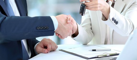 Ein Händedruck zwischen zwei Personen, bei dem die eine Person der anderen einen Autoschlüssel übergibt.