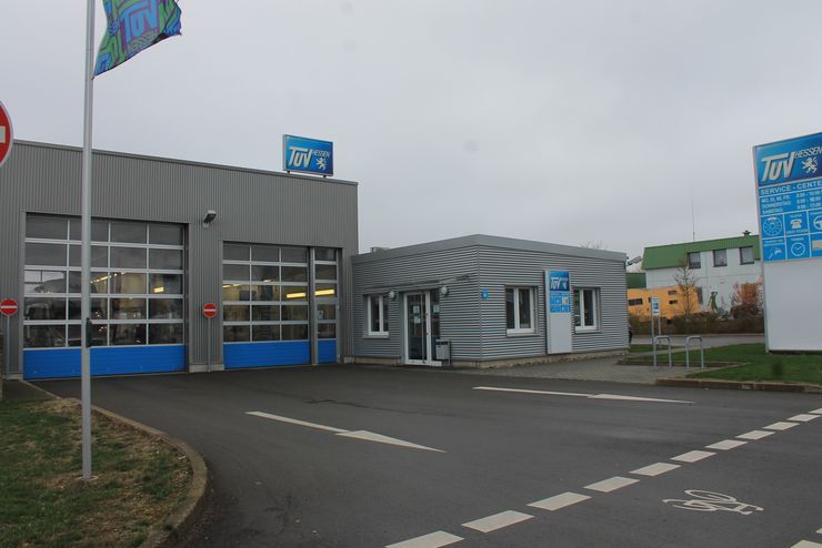 Ein modernes Gebäude mit einem blau-weißen "TUEV Hessen"-Logo, einem Schild mit verschiedenen Dienstleistungen.