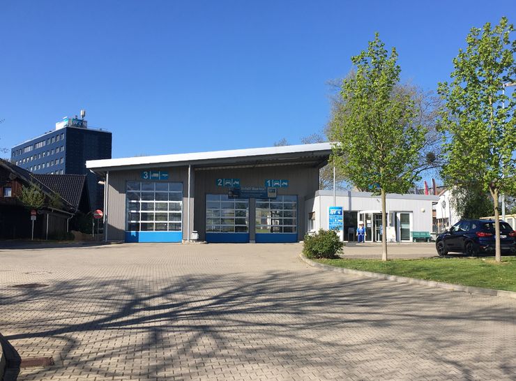 Eine moderne Autowaschanlage mit blauem und weißem Branding in einer städtischen Umgebung mit einem Gebäude im Hintergrund und einem draußen geparkten Auto.
