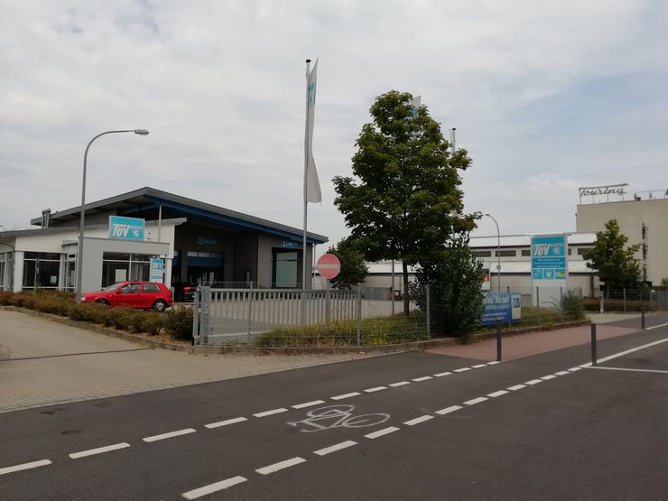 Ein modernes Gebäude mit blau-weißer Fassade, ein rotes Auto, das draußen parkt, ein Fahrradweg und ein paar Bäume.