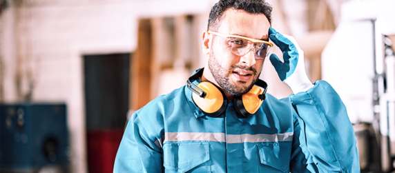Ein Mann in einer blauen Arbeitsuniform, mit Schutzbrille und Handschuhen, stellt seine Kopfhörer ein.