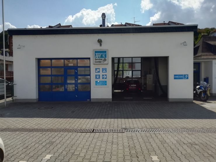 Ein weißes Gebäude mit blauen Türen, einem Schild mit der Aufschrift "TUEV Hessen Service Center" und einem vor dem Gebäude geparkten Motorrad.