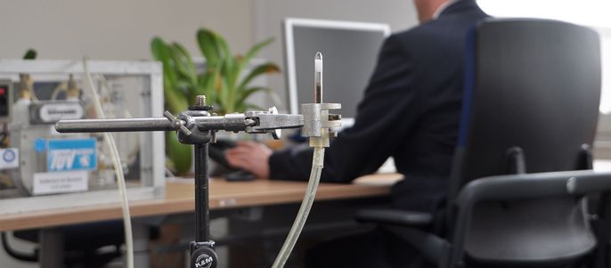 Ein Arbeitsbereich mit einem Metallständer, der eine Sonde hält, einem Computermonitor und einer Person in einem Anzug, die daran arbeitet.