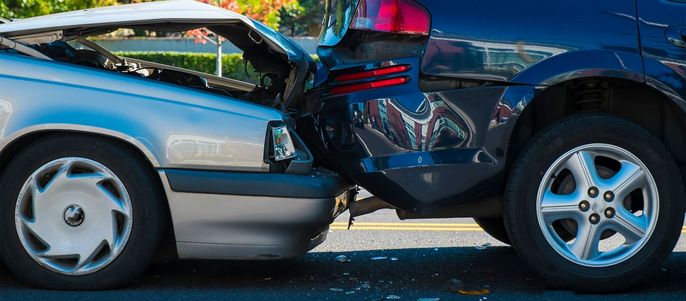 Zwei Autos, die zusammengestoßen sind, wobei die vordere Stoßstange und die Motorhaube des einen Autos beschädigt wurden und die hintere Stoßstange und die Seitenwand des anderen Autos ebenfalls betroffen sind.