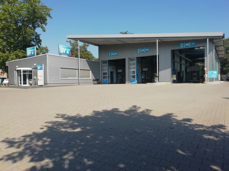 Eine moderne Autotankstelle mit TUEV Hessen Branding, drei Garagentoren und einem gepflasterten Parkplatz.