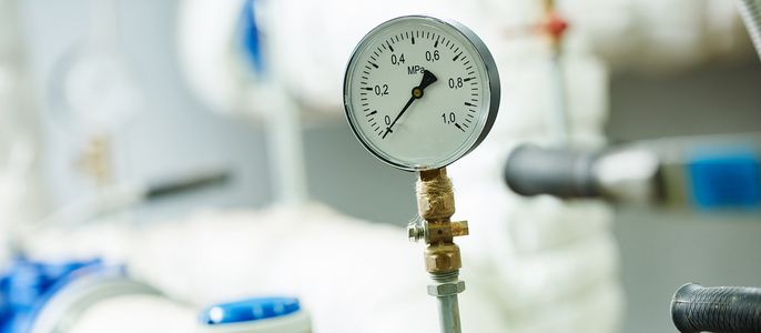 Ein Druckmessgerät mit einer Skala von 0 bis 6 MPa, das an ein System von Leitungen und Ventilen angeschlossen ist.