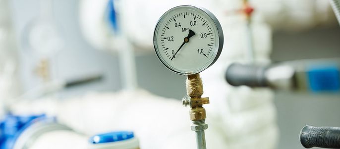 Ein Druckmessgerät mit einer Skala von 0 bis 6 MPa, das an ein System von Leitungen und Ventilen angeschlossen ist.