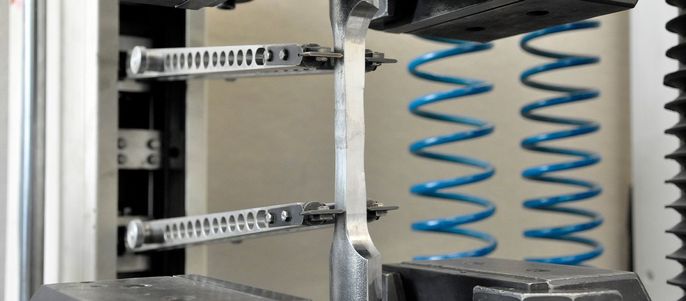 Eine mechanische Vorrichtung mit Metallteilen, einschließlich zwei Federn und Klammern, die an einer Wand befestigt ist.