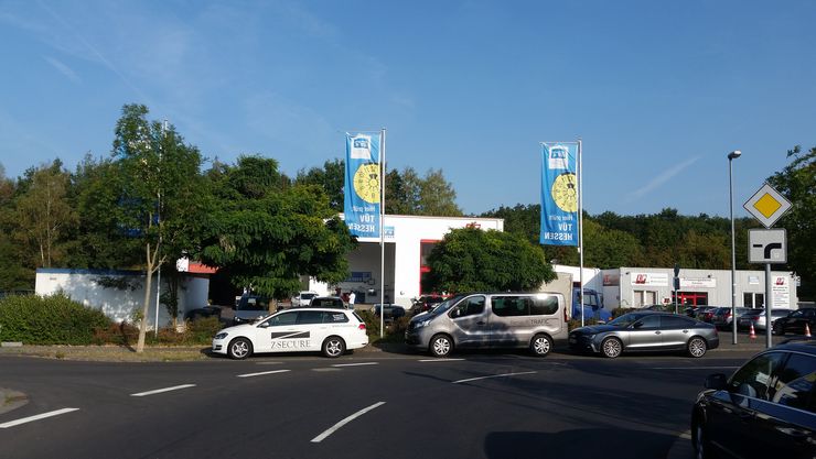 Eine Straßenszene mit einer Tankstelle, einigen Autos und Werbebannern für den TUEV Hessen.