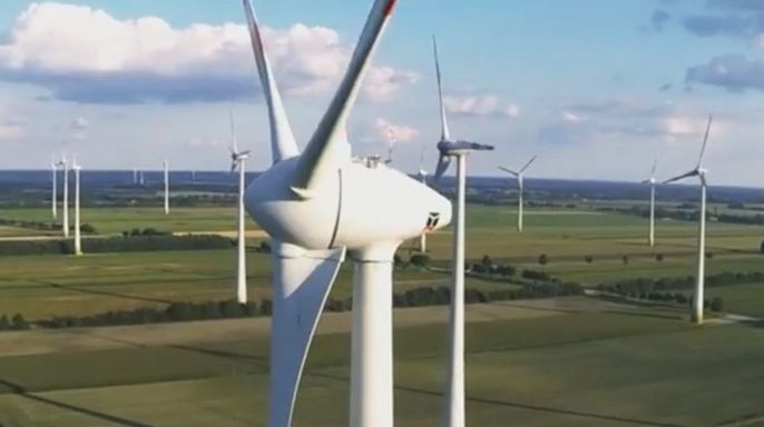 Eine weite Landschaft mit zahlreichen Windturbinen, die sich vor dem Hintergrund des blauen Himmels und der grünen Felder erheben.