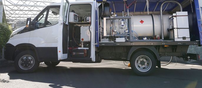 Ein weißer Lastwagen mit einem großen Tank auf dem Rücken, der mit verschiedenen Werkzeugen und Maschinen ausgestattet ist, parkt auf einer offenen Fläche.