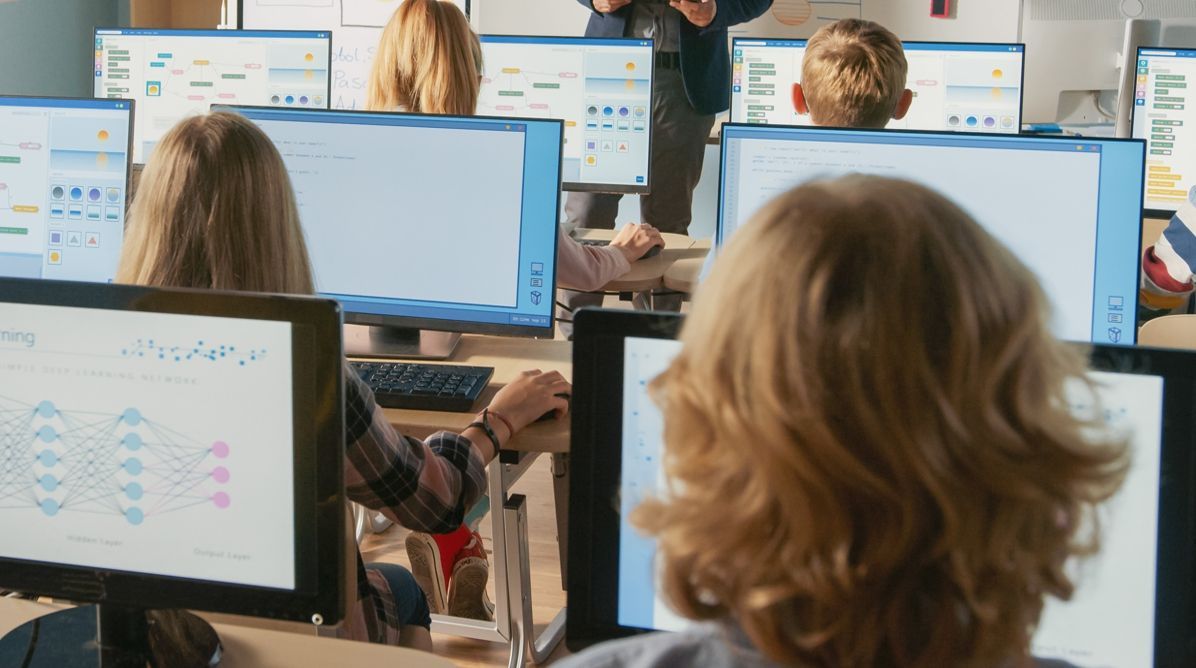 Ein Klassenzimmer, in dem die Schüler vor Computern sitzen, auf denen jeweils ein Diagramm zum Thema "Deep Learning" angezeigt wird.