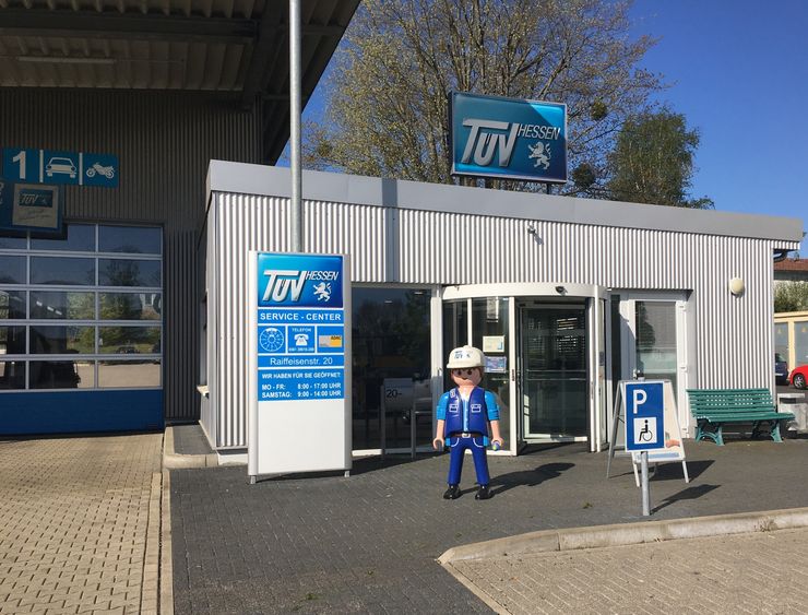 Ein Service-Center mit dem Namen "TUEV HESSEN" mit einem TUEV Hessen Playmobil Mann davor, das Autoservice und Inspektionen anbietet.